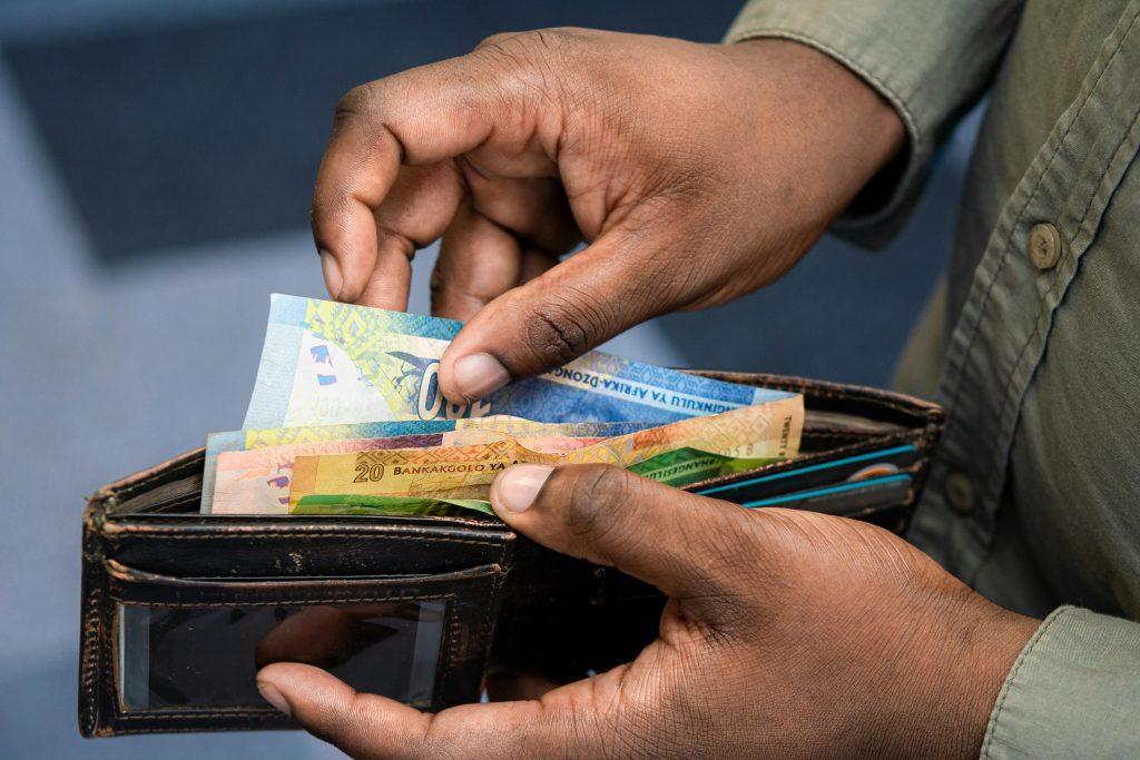 A person counting South African Rand from a wallet, symbolizing personal finance and wealth management.
