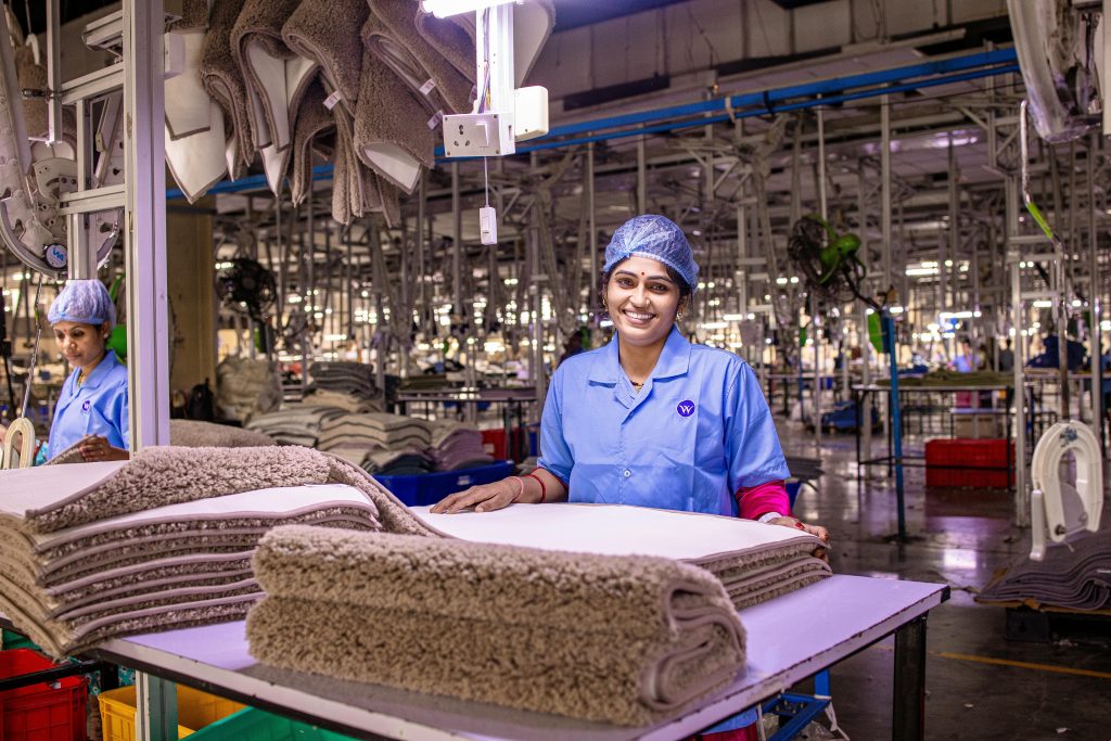 A smiling female worker in a textile factory, handling fabric with care.