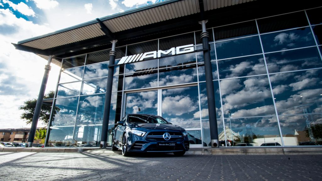 A sleek blue Mercedes-Benz parked outside the AMG showroom reflecting a cloudy sky.